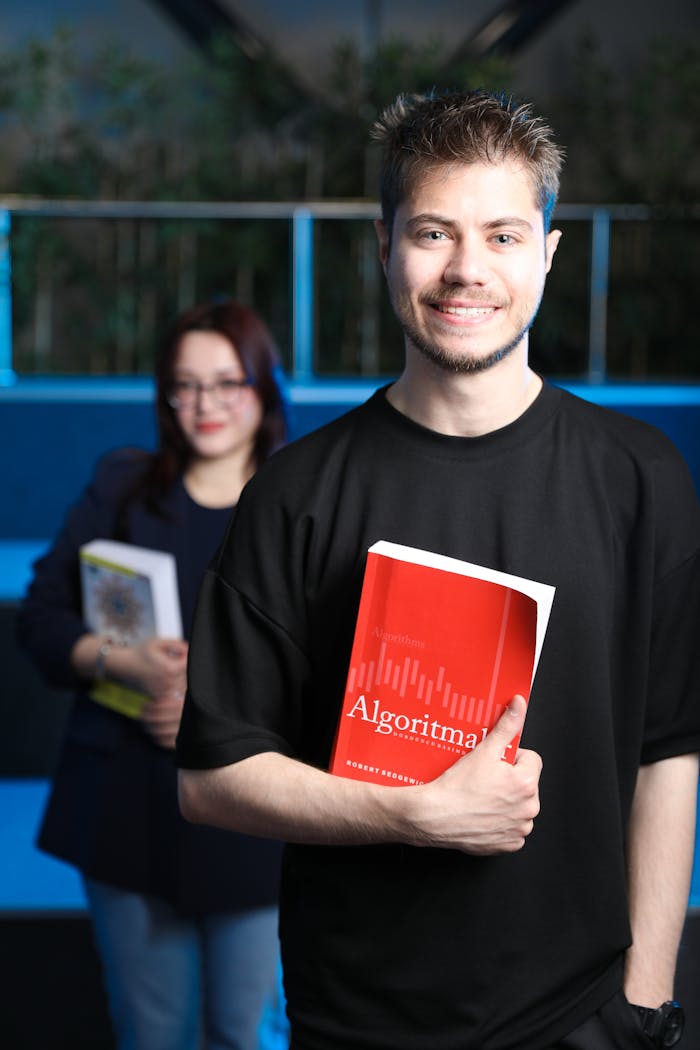 Two adults holding algorithm-themed books, smiling indoors with a tech-inspired theme.